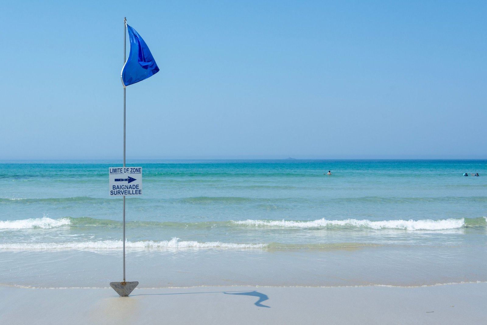 Tranquil beach with a blue flag and safety sign, perfect for summer travel.