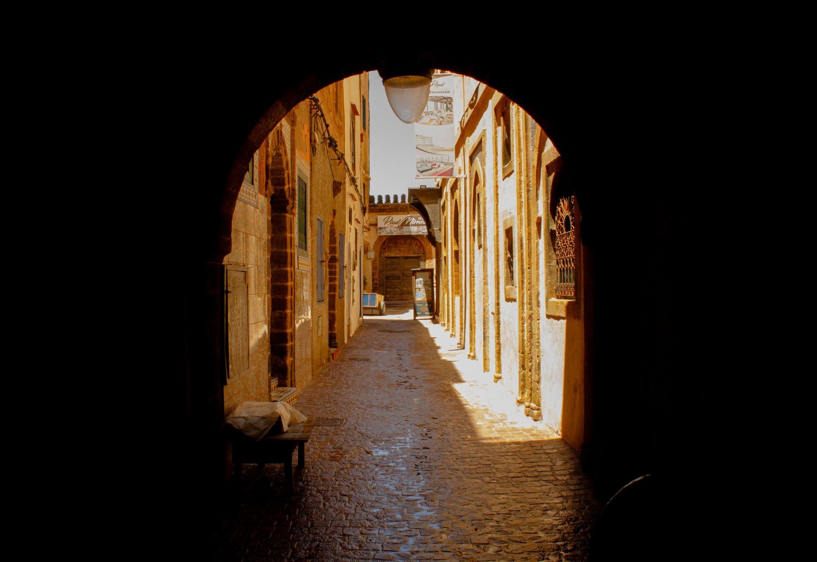 A sunlit alleyway in Essaouira, Morocco, showcasing traditional architecture and shadow play.