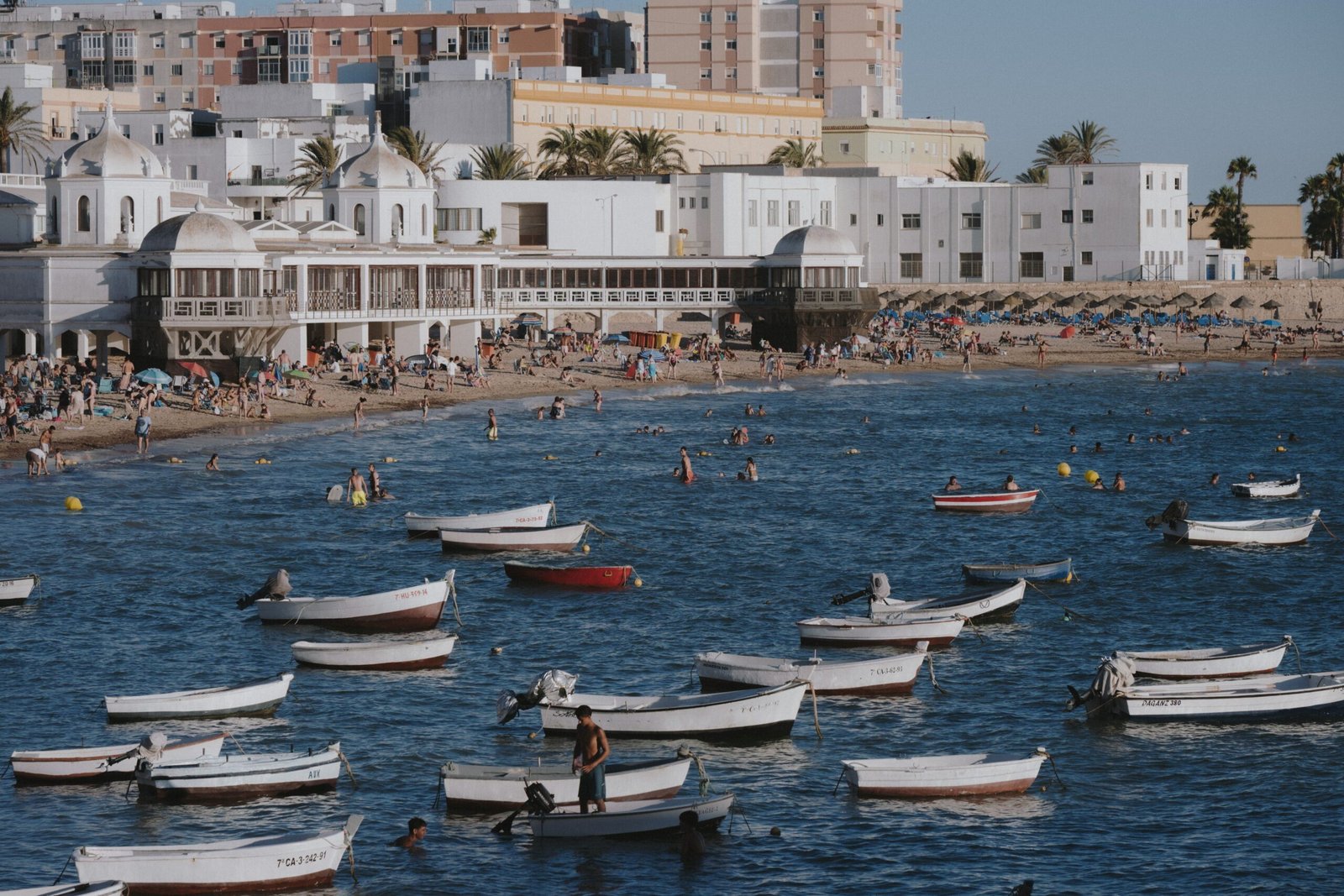 A lively beach scene with boats and people at La Caleta Beach, Cádiz, Spain.